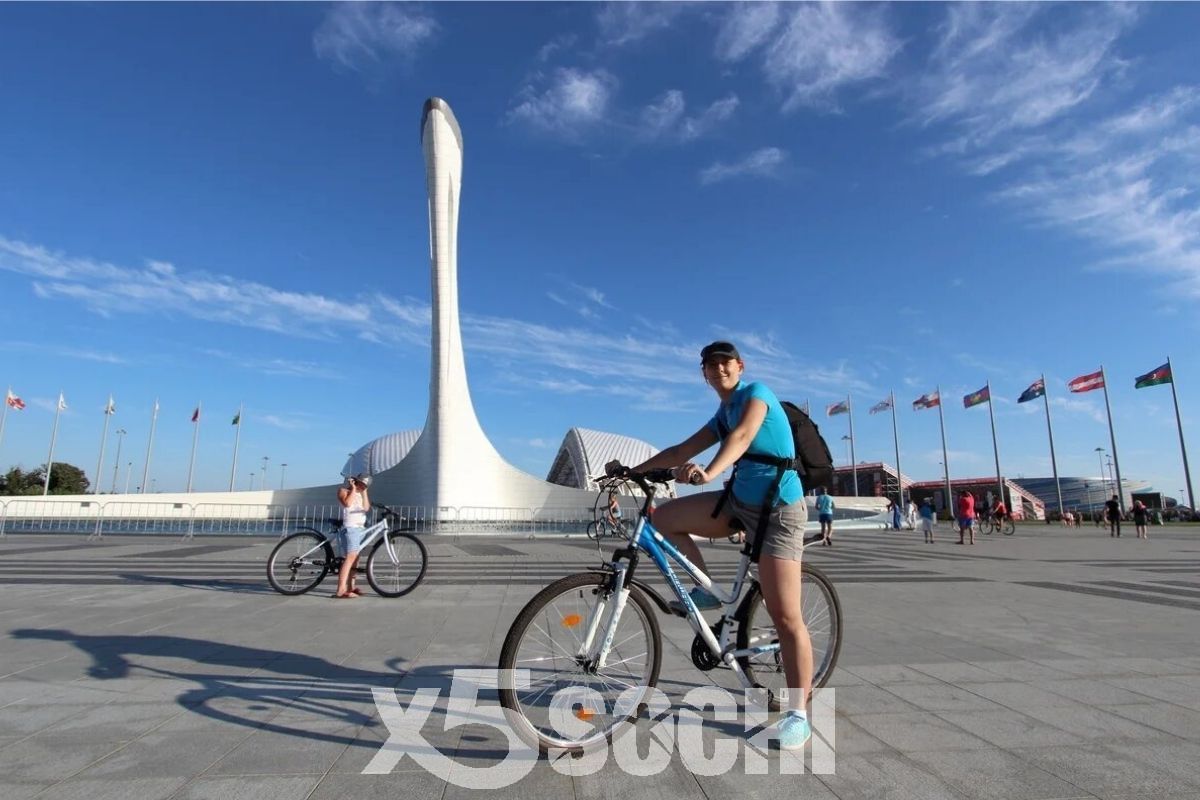Девушка на велосипеде на фоне олимпийской чаши в Сочи
